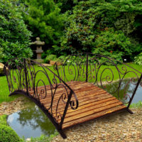 Ponte di legno con ringhiera forgiata sopra lo stagno del giardino