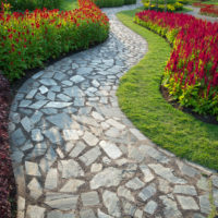 Пътека, изработена от естествен камък между цъфтящи цветни лехи