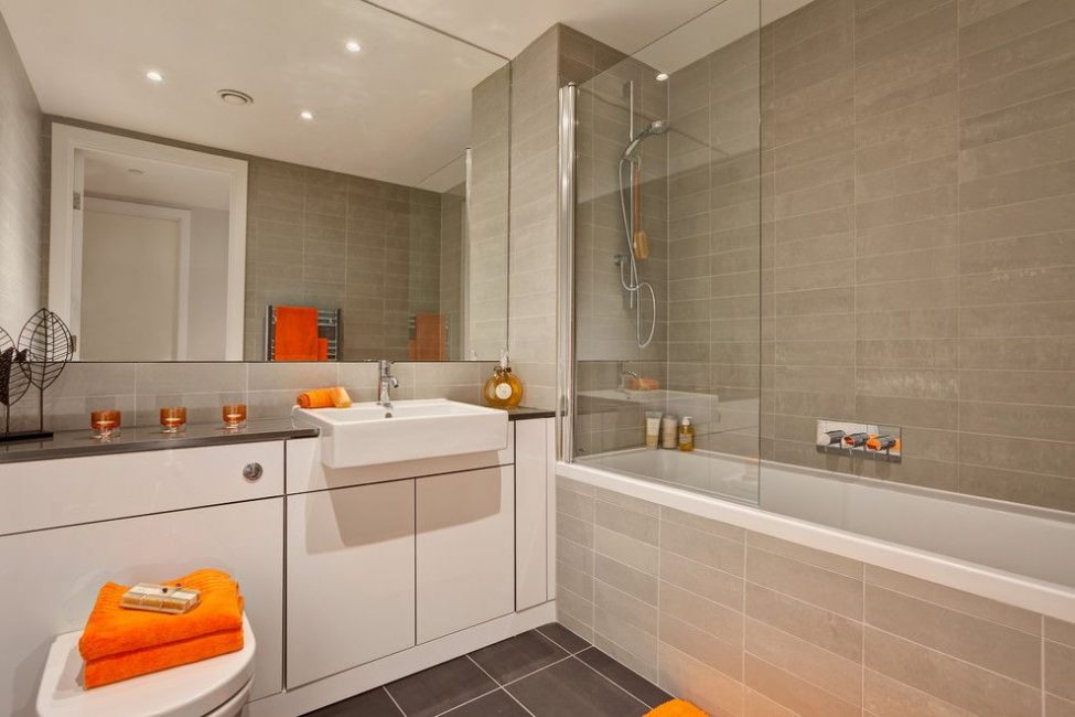 Oranžinis rankšluostis vonios kambaryje su dideliu veidrodžiu