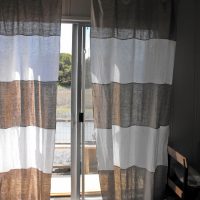 Miegamojo langas su pilkomis ir baltomis užuolaidomis