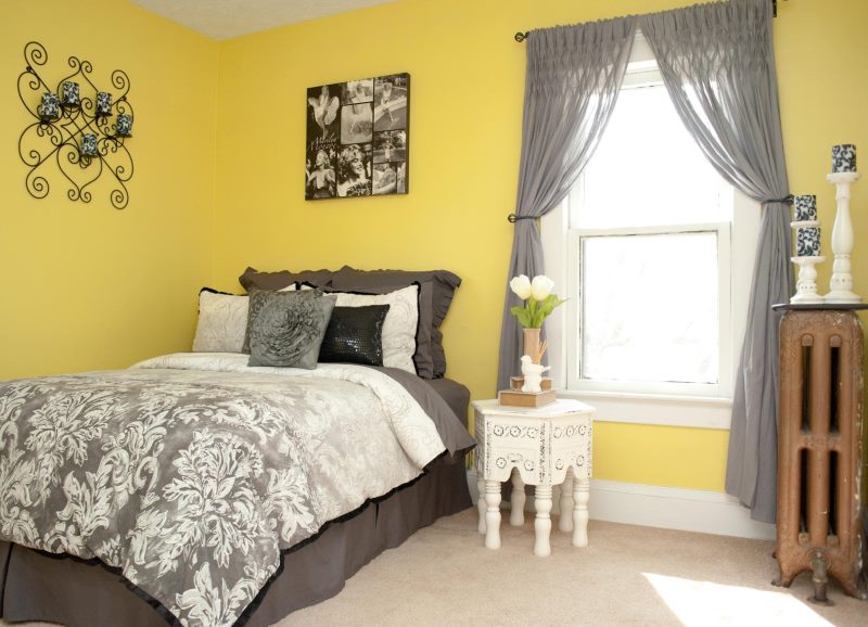 Permatomos pilkos užuolaidos miegamajame su geltonomis sienomis